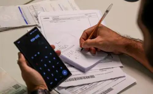 Pessoa calculando dívidas com celular e boletos em mãos