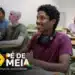 Estudantes em sala de aula com um jovem sorrindo e utilizando um laptop, participando de um ambiente de aprendizagem.