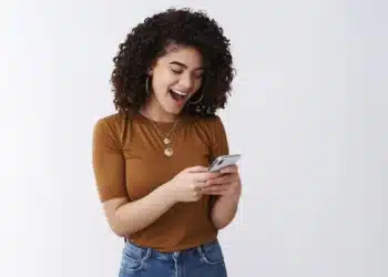 Mulher sorrindo enquanto usa o celular, simbolizando o uso de aplicativos para antecipação de salário.