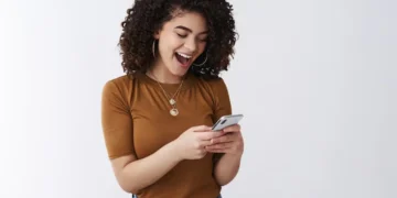 Mulher sorrindo enquanto usa o celular, simbolizando o uso de aplicativos para antecipação de salário.