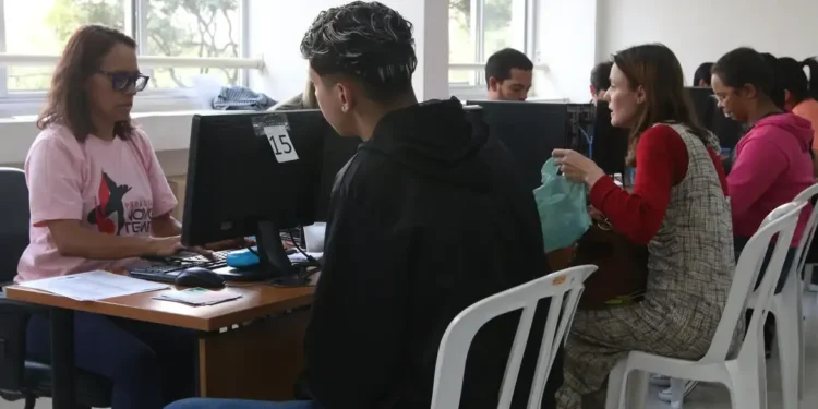 Pessoas sendo atendidas em guichês de assistência social com uso de computador