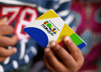 Cartão do Programa Bolsa Família sendo segurado por uma mão, com fundo colorido e texto sobre revisão de cadastro.