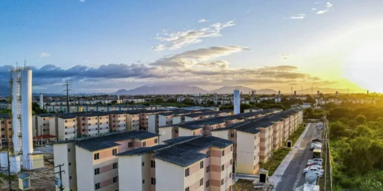 Vista aérea de conjunto habitacional do programa Minha Casa Minha Vida, com várias unidades residenciais e a luz do pôr do sol ao fundo.