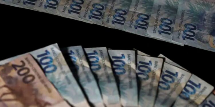 Pessoa contando cédulas de 100 reais sobre fundo escuro