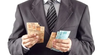 Homem de terno segurando notas de 50 e 100 reais, representando formas de ganhar dinheiro.