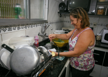 Dona de casa lavando louça, tema sobre como contribuições para o INSS garantem aposentadoria e benefícios.