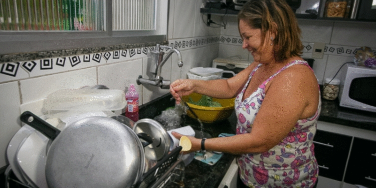 Dona de casa lavando louça, tema sobre como contribuições para o INSS garantem aposentadoria e benefícios.