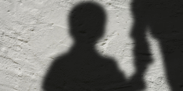 Silhueta de uma criança segurando a mão de um adulto, representando o auxílio para órfãos de feminicídio.