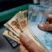 Notas de reais sendo retiradas de um caixa eletrônico, relacionadas ao debate sobre o salário mínimo ideal em 2025 segundo o Dieese.