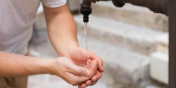 Homem com as mãos abertas recebendo água da torneira, simbolizando a economia proporcionada pela nova tarifa social em SP.