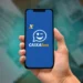 Pessoa segura celular com aplicativo Caixa Tem aberto, com notas de R$ 100 ao fundo