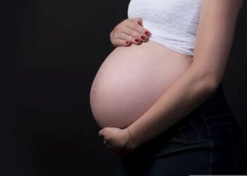 Mulher grávida segurando a barriga em fundo escuro, simbolizando o salário-maternidade para autônomas