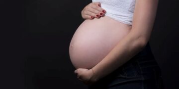 Mulher grávida segurando a barriga em fundo escuro, simbolizando o salário-maternidade para autônomas