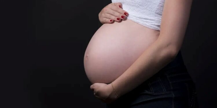 Mulher grávida segurando a barriga em fundo escuro, simbolizando o salário-maternidade para autônomas