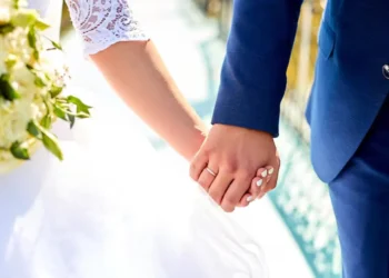 Casal de noivos segurando as mãos durante o casamento, com destaque para os anéis de compromisso.