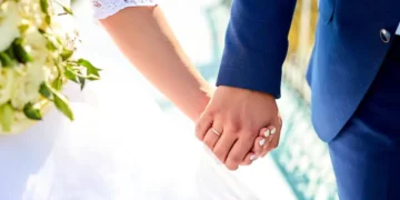 Casal de noivos segurando as mãos durante o casamento, com destaque para os anéis de compromisso.