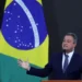Ministro Rui Costa discursando sobre a desvinculação do salário mínimo da aposentadoria, com a bandeira do Brasil ao fundo.