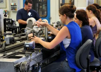Trabalhadores em uma linha de montagem, realizando atividades em um ambiente industrial, com foco em mulheres no trabalho.
