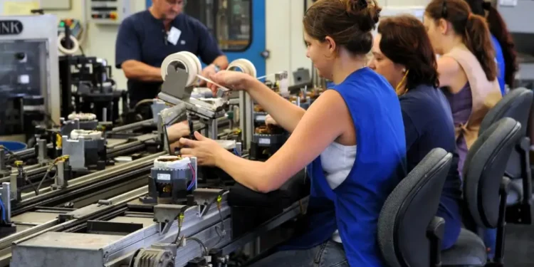 Trabalhadores em uma linha de montagem, realizando atividades em um ambiente industrial, com foco em mulheres no trabalho.