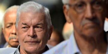 Homem idoso de cabelos brancos participando de evento ao ar livre, com expressão serena