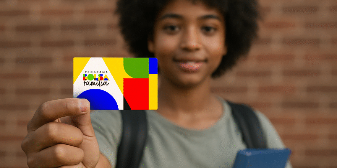 Jovem segurando o cartão do programa Bolsa Família com sorriso, em frente a um fundo de tijolos.