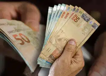 Notas de 50 reais sendo seguradas por mãos, representando dinheiro em espécie.