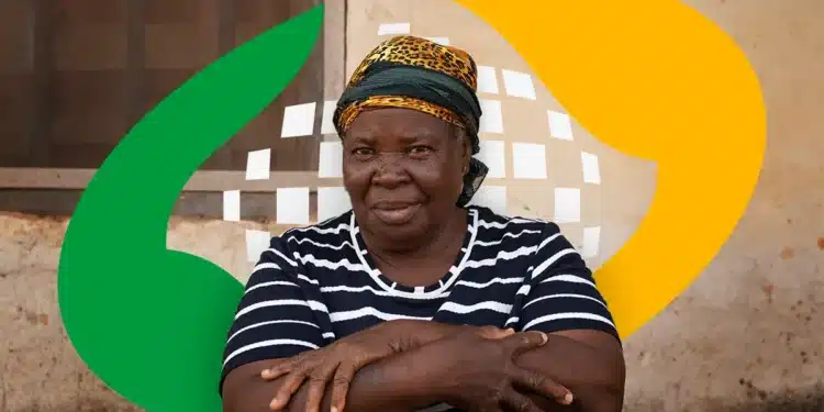 Mulher idosa, vestindo uma blusa listrada, com braços cruzados e expressão séria, contra um fundo de parede com elementos gráficos de cores verde e amarela. Imagem relacionada à prova de vida no INSS.