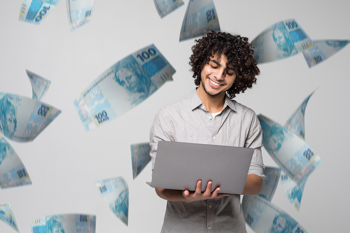 Pessoa sorrindo com um laptop enquanto cédulas de dinheiro caem ao fundo, representando o impacto do novo salário mínimo de R$ 1.804