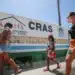 Atendimento do CRAS suspenso com pessoas caminhando em frente ao centro, buscando informações sobre os serviços.