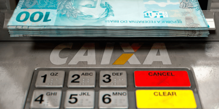 Caixa eletrônico dispensando cédulas de R$ 100. Depósitos de R$ 2.800 para brasileiros com CPF final 0 a 9 em agosto.