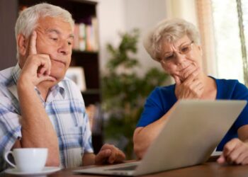 Casal de idosos analisa informações no notebook enquanto planeja decisões financeiras para a aposentadoria.