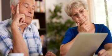 Casal de idosos analisa informações no notebook enquanto planeja decisões financeiras para a aposentadoria.