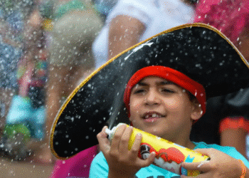 Criança com chapéu de pirata segurando spray em evento festivo ao ar livre.