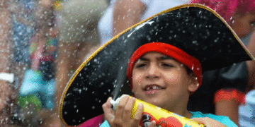 Criança com chapéu de pirata segurando spray em evento festivo ao ar livre.