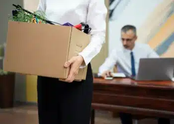 Funcionária carregando caixa de objetos pessoais após demissão sem justa causa.