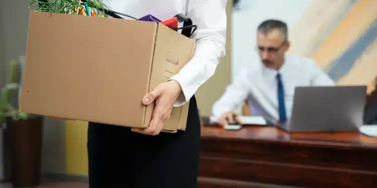 Funcionária carregando caixa de objetos pessoais após demissão sem justa causa.