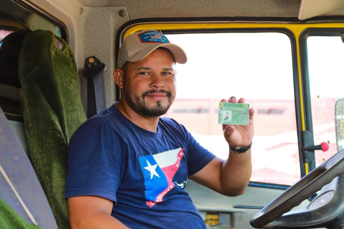 Motorista sorrindo dentro do caminhão, exibindo sua CNH como parte do programa de CNH grátis do Detran.