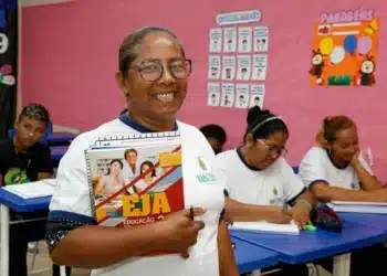 Aluna sorridente segurando caderno do EJA em sala de aula