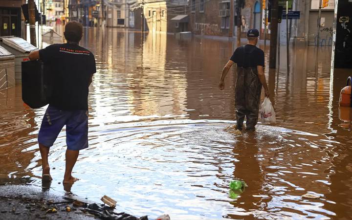 Cenas de enchente em rua alagada com moradores caminhando na água, representando os impactos de desastres naturais para o saque de calamidade FGTS.