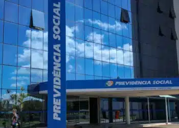 Fachada do INSS com reflexo do céu em vidros, destacando o logo da Previdência Social.