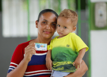 Imagem de mãe segurando criança com cartão do programa Mães de Pernambuco, que abre 1.700 vagas em agosto.