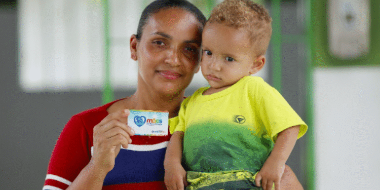 Imagem de mãe segurando criança com cartão do programa Mães de Pernambuco, que abre 1.700 vagas em agosto.