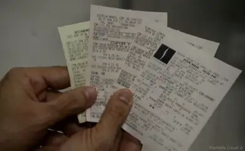  Mão segurando várias notas fiscais impressas