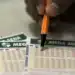 Pessoa preenchendo um bilhete da Mega-Sena com caneta laranja.