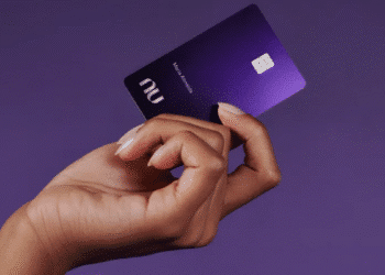 Cartão Nubank Ultravioleta sendo segurado por mão feminina contra fundo roxo.