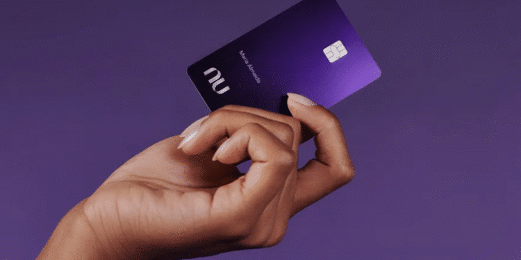 Cartão Nubank Ultravioleta sendo segurado por mão feminina contra fundo roxo.