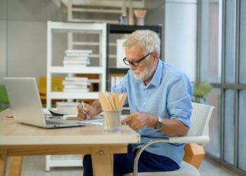 Homem idoso trabalhando em escritório com laptop e documentos sobre a mesa