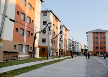 Prédios residenciais com apartamentos em um condomínio do programa Minha Casa, Minha Vida, em uma rua com pessoas caminhando.