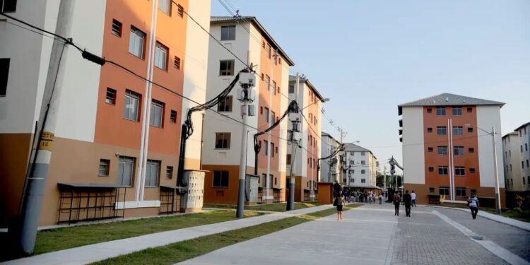 Prédios residenciais com apartamentos em um condomínio do programa Minha Casa, Minha Vida, em uma rua com pessoas caminhando.