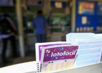 Bilhete da Lotofácil em destaque na lotérica, com pessoas ao fundo aguardando atendimento.